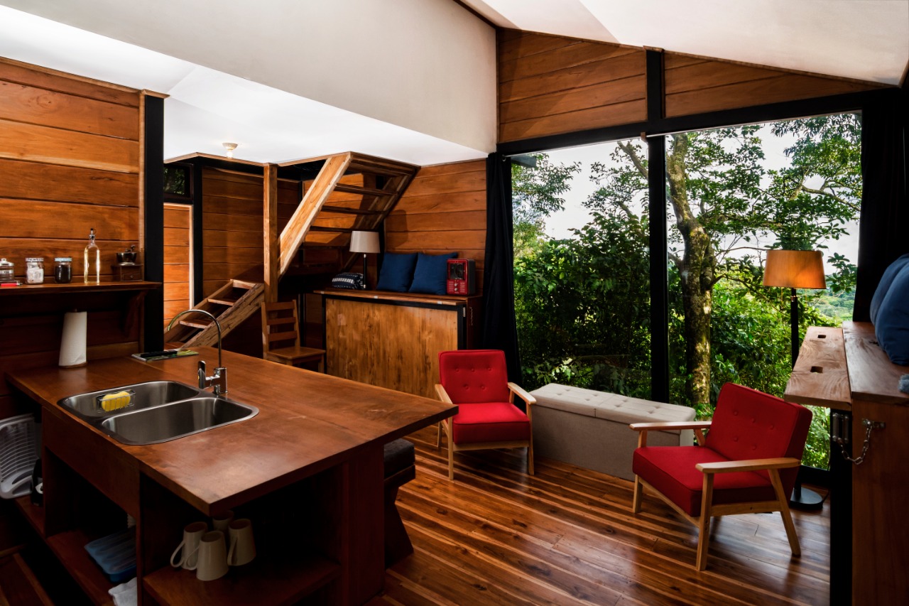 Sala y cocina de la Guest House con ventanal de piso a techo hacia el bosque nuboso