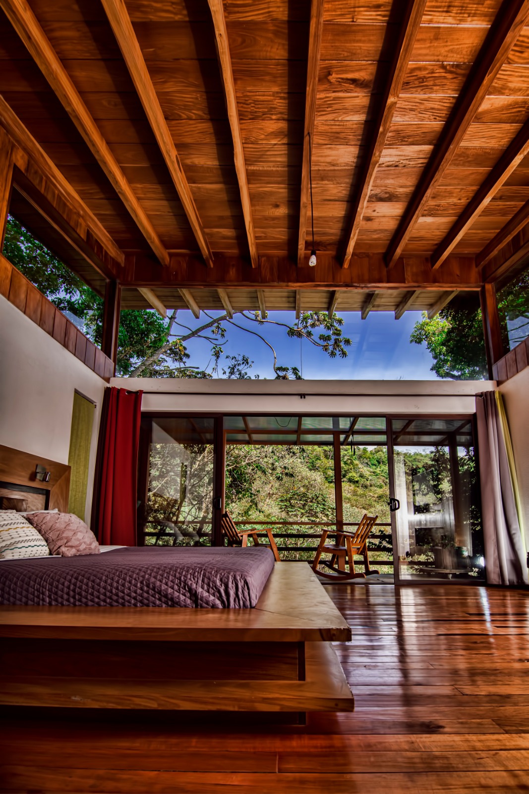 Dormitorio de Casa Ficus con ventanal de piso a techo y terraza con mecedoras sobre el bosque